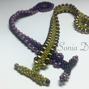 May include: A beaded bracelet with a green and purple colour gradient. The bracelet is made with small, round beads and has a clasp closure. The bracelet is designed in a zig-zag pattern.