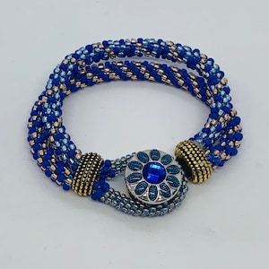 May include: A blue and silver beaded bracelet with a flower-shaped clasp. The bracelet is made with multiple strands of beads in shades of blue and silver.