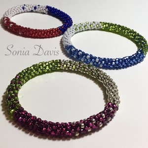 Op de afbeelding: Drie kralenarmbanden met verschillende kleurcombinaties. De bovenste armband is rood, wit en blauw. De middelste armband is wit, groen en blauw. De onderste armband is groen, zilver en roze.