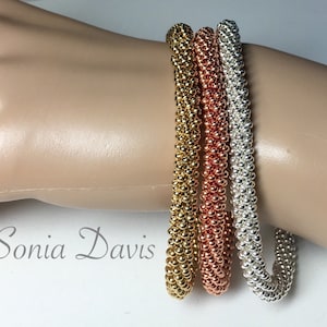 May include: Three beaded bracelets in gold, copper, and silver. The bracelets are stacked on a mannequin's wrist.