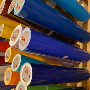 May include: A collection of colorful vinyl rolls, including shades of blue, yellow, orange, and green. The rolls are neatly stacked, with the brand name "ORAFOL" visible on the labels. The image showcases a variety of vinyl colors.