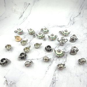 May include: A collection of miniature tea sets, including teapots, cups, and saucers. Some teapots are silver-toned, while others feature floral designs with green, white, and red accents. The cups and saucers are also silver-toned.