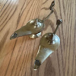 May include: Two silver metal genie lamps with chains. The lamps are shaped like a traditional oil lamp with a spout and a handle.