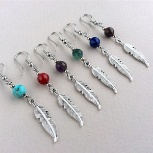 May include: Six pairs of dangle earrings with silver-colored feather charms. Each earring features a different colored bead: turquoise, red, purple, green, blue, and brown. The earrings have silver-colored hooks.