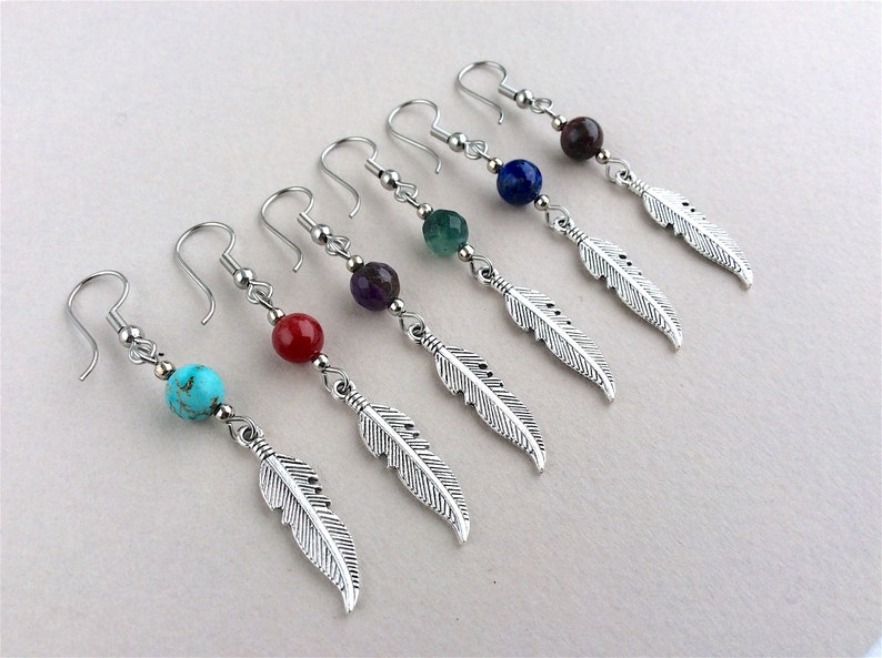 May include: Six pairs of dangle earrings with silver-colored feather charms. Each earring features a different colored bead: turquoise, red, purple, green, blue, and brown. The earrings have silver-colored hooks.