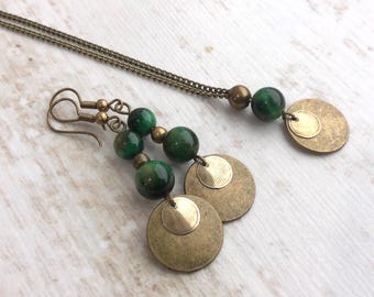 Puede incluir: Un par de pendientes colgantes y un collar a juego con cuentas esféricas de color verde oscuro y discos metálicos circulares en tono latón. Los pendientes tienen ganchos y el collar consta de una fina cadena metálica con cuenta y disco.