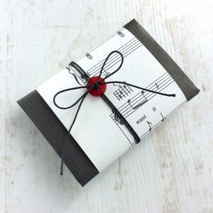 May include: A small, rectangular package wrapped in black paper and sheet music. A red button and black string are used to secure the package. The sheet music has the words "want it" printed on it.