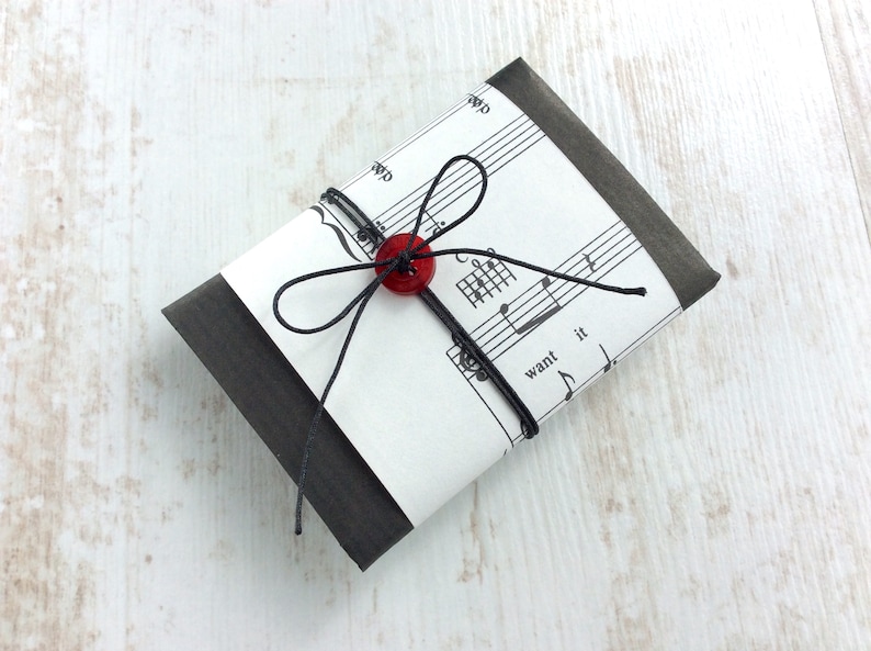 May include: A small, rectangular package wrapped in black paper and sheet music. A red button and black string are used to secure the package. The sheet music has the words "want it" printed on it.