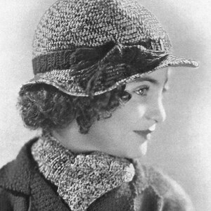 May include: A black and white photo of a young woman wearing a crocheted hat with a wide brim and a matching crocheted scarf. The hat has a black ribbon around the crown and a bow on the side.