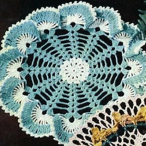 May include: A crocheted doily with a blue and white design. The doily has a circular shape with a center that is white and a border that is blue. The doily is made with a delicate stitch pattern.
