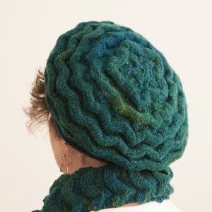 May include: A green and blue knitted beret with a cable knit pattern. The beret is worn on a person's head.