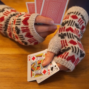 May include: Two hands wearing white and red patterned fingerless gloves hold a deck of playing cards. The cards are face up and show the King of Diamonds and the King of Spades.