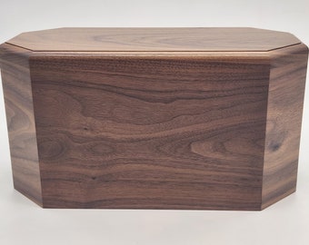Könnte beinhalten: Eine dunkelbraune Holzkiste mit rechteckiger Form und einem leicht erhöhten Deckel. Die Kiste hat eine glatte, polierte Oberfläche und ist aus massivem Holz gefertigt.
