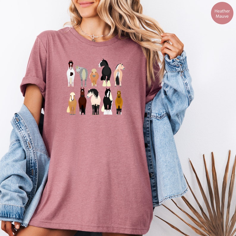 Pode incluir: Uma camiseta de cor malva desbotada com um gr&aacute;fico de nove cavalos diferentes em v&aacute;rias cores e poses. Os cavalos est&atilde;o todos olhando para a frente e est&atilde;o em p&eacute; sobre um fundo branco.