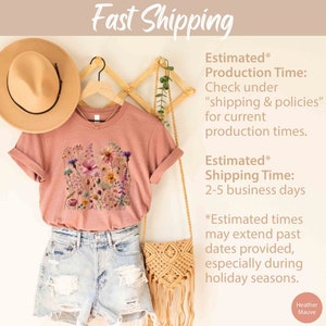 K&ouml;nnte beinhalten: Ein T-Shirt in Heide-Mauve mit einem floralen Druckdesign. Das T-Shirt h&auml;ngt an einem Holzb&uuml;gel. Der Text "Fast Shipping" befindet sich oben im Bild. Der Text "Estimated* Production Time: Check under "shipping & policies" for current production times." befindet sich rechts im Bild. Der Text "Estimated* Shipping Time: 2-5 business days" befindet sich rechts im Bild. Der Text "*Estimated times may extend past dates provided, especially during holiday seasons." befindet sich rechts im Bild. Der Text "Heather Mauve" befindet sich unten rechts im Bild.