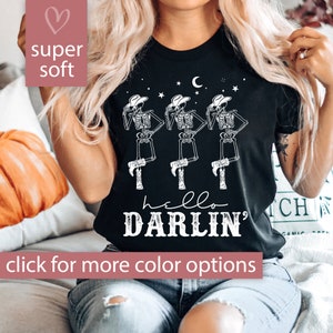 May include: Black t-shirt with a white graphic of three skeletons wearing cowboy hats and boots. The text "hello darlin'" is printed below the skeletons.