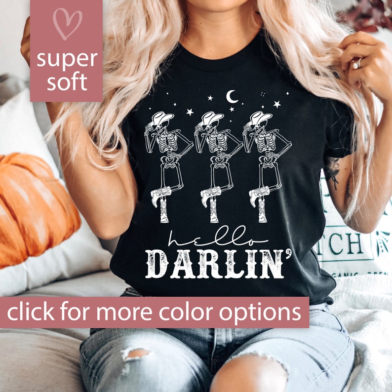 May include: Black t-shirt with a white graphic of three skeletons wearing cowboy hats and boots. The text "hello darlin'" is printed below the skeletons.
