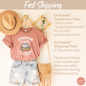 May include: A heather mauve t-shirt with a white graphic of a cinnamon roll and the text "Synonym Rolls" and "Just like grammar used to make".