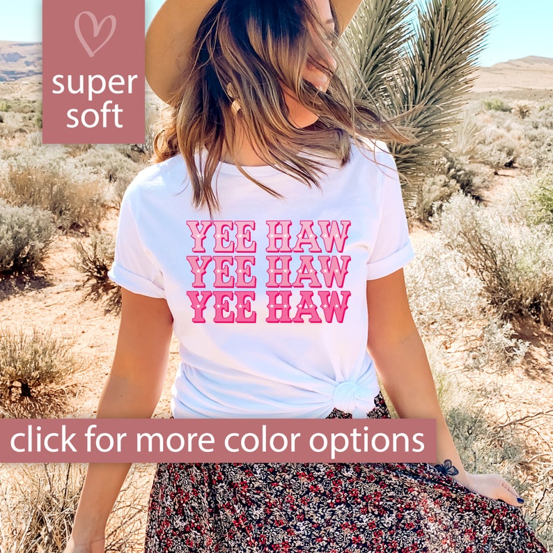 May include: White t-shirt with the phrase "Yee Haw" repeated three times in pink with a gradient effect. The shirt is being worn by a person in a desert setting.