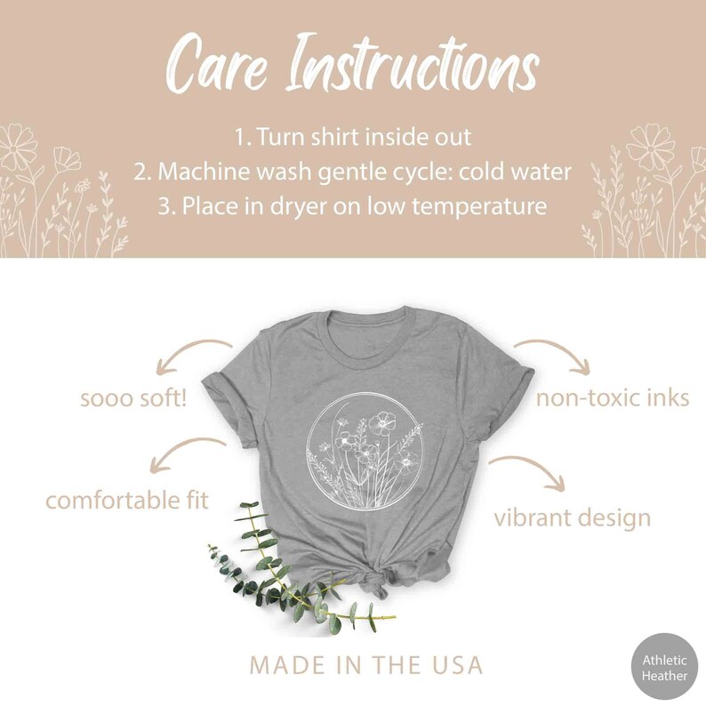 May include: A gray t-shirt with a white floral design in a circle. The shirt is made in the USA and features non-toxic inks. The text "sooo soft!" and "comfortable fit" are written on the left side of the image. The text "non-toxic inks" and "vibrant design" are written on the right side of the image. The text "Care Instructions" is at the top of the image with instructions for washing and drying the shirt. The text "MADE IN THE USA" is at the bottom of the image.