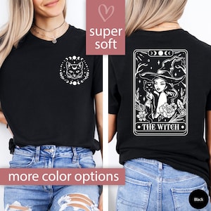 May include: Black t-shirt with a white cat and moon phases design on the front. The back features a tarot card design with a witch and cat, with the text "THE WITCH". The shirt is labeled "super soft" and "more color options".