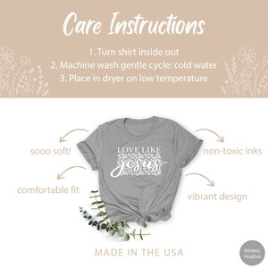 Pode incluir: Uma camiseta cinza com um gr&aacute;fico branco que diz "LOVE LIKE JESUS" em um design de estampa de leopardo. A camiseta &eacute; feita nos EUA e apresenta um caimento confort&aacute;vel, um tecido macio e tintas n&atilde;o t&oacute;xicas.