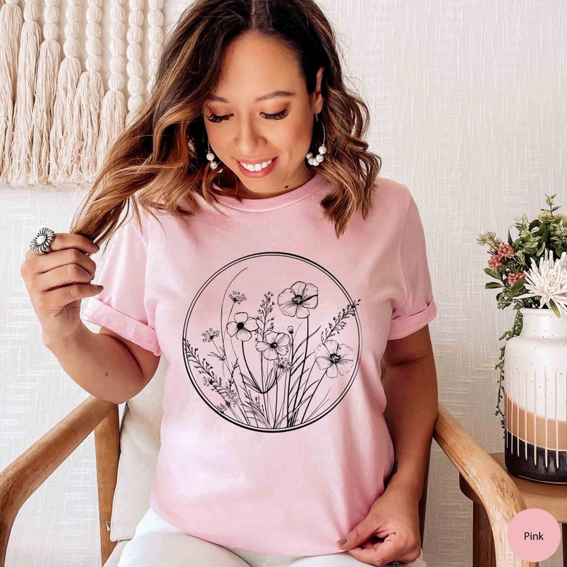May include: A pink t-shirt with a black and white graphic of flowers in a circle. The flowers are stylized and have a minimalist design.