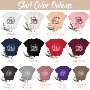 May include: A selection of t-shirts in various colors, each featuring a white graphic of a football with the text "FOOTBALL mom". The colors include white, natural, heather peach, pink, navy, black, red, maroon, grey heather, athletic heather, heather mauve, team purple, and heather olive.