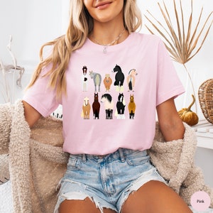 Pode incluir: Uma camiseta rosa com um gr&aacute;fico de v&aacute;rios cavalos em diferentes cores e poses. Os cavalos est&atilde;o todos olhando para o espectador e t&ecirc;m as caudas levantadas.