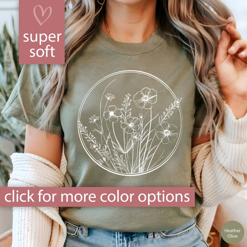 May include: A green t-shirt with a white outline of flowers and leaves in a circle. The text "super soft" is on the top left of the image. The text "click for more color options" is at the bottom of the image.