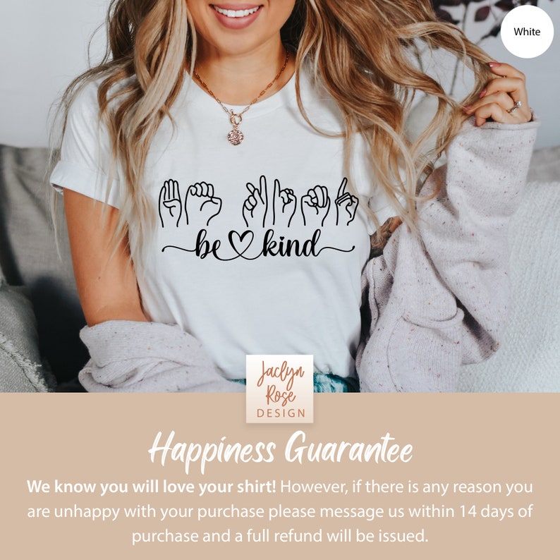 May include: White t-shirt with a black design that says "be kind" in sign language. The design includes a heart symbol. The shirt is being worn by a person.