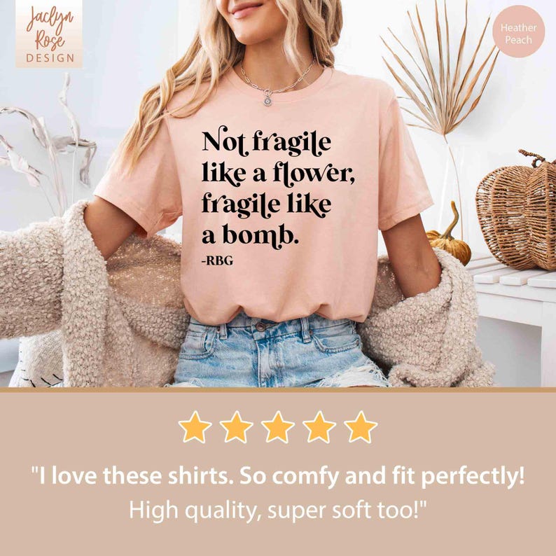 May include: A pink t-shirt with the text "Not fragile like a flower, fragile like a bomb. -RBG" printed on it. The shirt is being worn by a person. The shirt has a five-star rating and the text "I love these shirts. So comfy and fit perfectly! High quality, super soft too!"