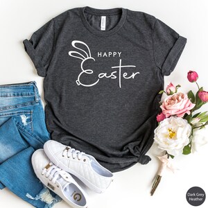 May include: A dark grey heather t-shirt with a white bunny ear design and the text "Happy Easter".