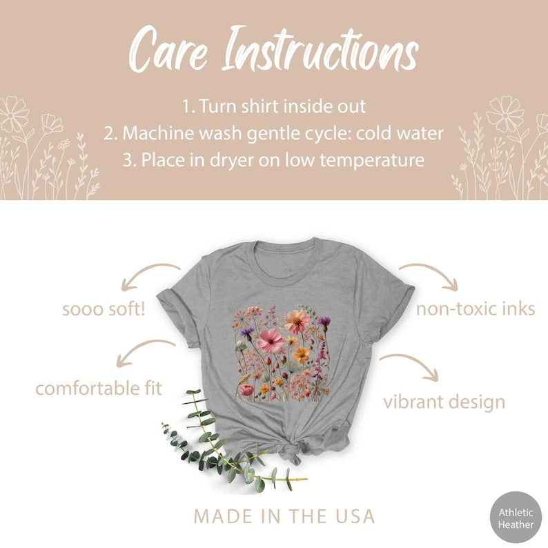 K&ouml;nnte beinhalten: Ein graues T-Shirt mit einem floralen Druckdesign. Das Shirt ist in den USA hergestellt und verwendet nicht-toxische Farben. Der Text "sooo soft!" und "comfortable fit" steht auf der linken Seite des Bildes. Der Text "non-toxic inks" und "vibrant design" steht auf der rechten Seite des Bildes. Der Text "MADE IN THE USA" steht am unteren Rand des Bildes.