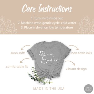 May include: A grey t-shirt with a white bunny and the text "Happy Easter" printed on the front. The shirt is made in the USA and is made of a soft, comfortable material. The shirt is shown on a white background with flowers and greenery.