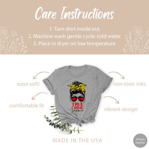 May include: Gray t-shirt with a graphic of a woman with a messy bun wearing sunglasses and a yellow "Do Not Cross" tape headband. The text "TRUE CRIME JUNKIE" is printed in red below the graphic. The shirt is made in the USA.