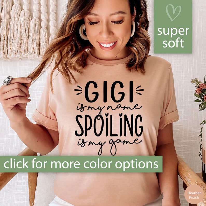 Op de afbeelding: Een perzikkleurig T-shirt met zwarte tekst die "GIGI is my name SPOILING is my game" luidt. Het shirt is superzacht en heeft een hartje in de rechterbovenhoek.