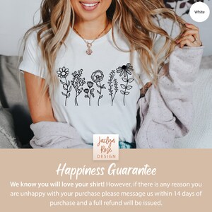May include: White t-shirt with a black line drawing of a row of flowers. The text "Jaclyn Rose DESIGN" is on the bottom of the shirt. The text "Happiness Guarantee" is on a tan background below the shirt. The text "We know you will love your shirt! However, if there is any reason you are unhappy with your purchase please message us within 14 days of purchase and a full refund will be issued." is below the text "Happiness Guarantee."