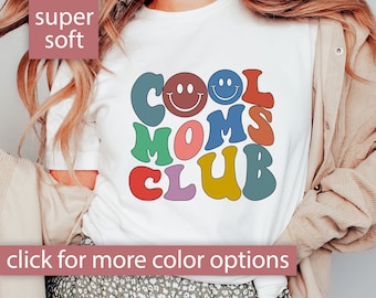 May include: White t-shirt with a colorful graphic that says "Cool Moms Club" with smiley faces. The graphic is in a retro style.