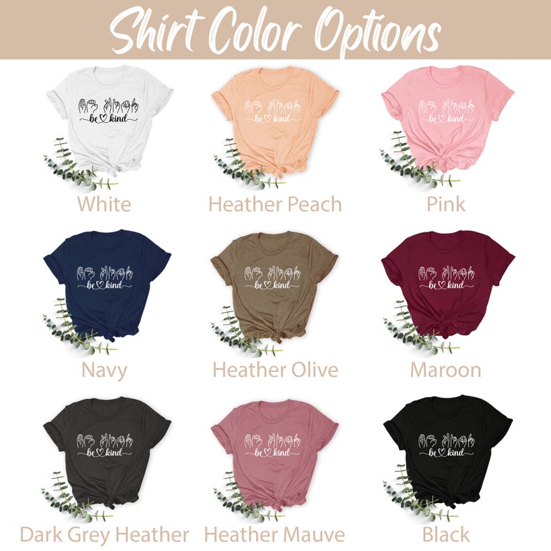 May include: A selection of t-shirts in various colors, including white, heather peach, pink, navy, heather olive, maroon, dark grey heather, heather mauve, and black. Each shirt features a white graphic of hands signing "be kind" with a heart.