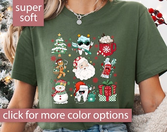 May include: A green t-shirt with a Christmas-themed design featuring a tooth character, Santa Claus, a snowman, a gingerbread man, a toothbrush, and a cup of hot chocolate. The text "super soft" is in a pink heart shape at the top of the image. The text "click for more color options" is at the bottom of the image.