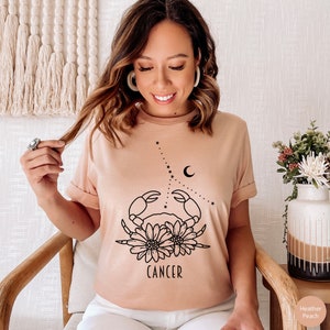 May include: A heather peach t-shirt with a black line drawing of a crab with flowers and the word "CANCER" underneath.