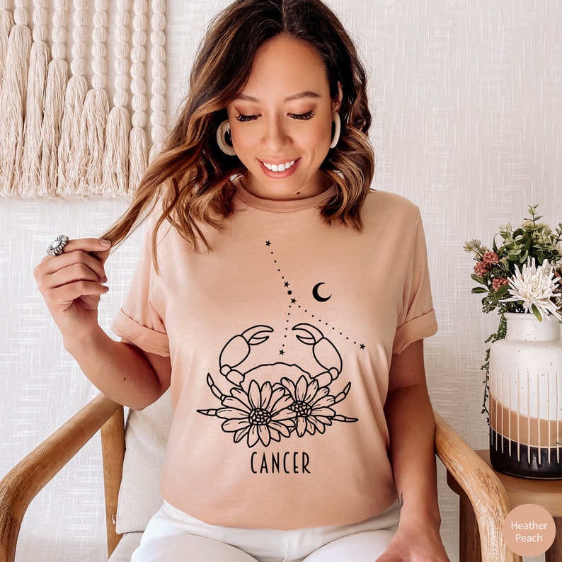 May include: A heather peach t-shirt with a black line drawing of a crab with flowers and the word "CANCER" underneath.