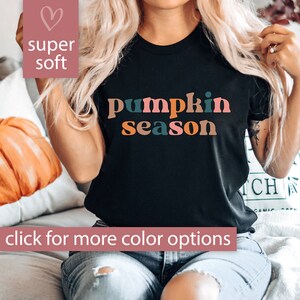 Puede incluir: Una camiseta negra con el texto "pumpkin season" en letras de colores. El texto est&aacute; en una fuente de estilo retro. La camiseta la lleva puesta una persona.