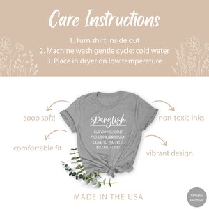 K&ouml;nnte beinhalten: Graues T-Shirt mit dem Text "Spanglish" und dem Satz "Cuando you can't find la palabra en un idioma so you fill it in con la otra". Das Shirt ist in den USA hergestellt und bietet eine bequeme Passform, weichen Stoff, ungiftige Tinten und ein lebendiges Design.