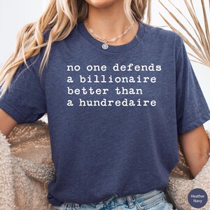 K&ouml;nnte beinhalten: Ein marineblaues T-Shirt mit wei&szlig;em Text, der "no one defends a billionaire better than a hundredaire" lautet.