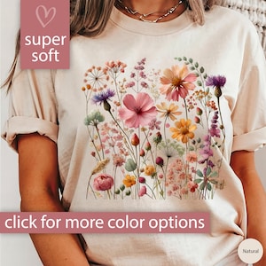 K&ouml;nnte beinhalten: Ein beiges T-Shirt mit einem Blumendruck mit rosa, gelben und violetten Blumen. Der Text "super soft" befindet sich in einem rosa Herz oben links im Bild. Der Text "Klicke f&uuml;r weitere Farboptionen" befindet sich unten im Bild.