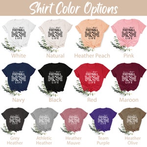 May include: A graphic t-shirt design featuring a football with the text "I'm that football mom" and "life" in black and white. The shirt is shown in 10 different colors: white, natural, heather peach, pink, navy, black, red, maroon, grey heather, athletic heather, heather mauve, team purple, and heather olive.
