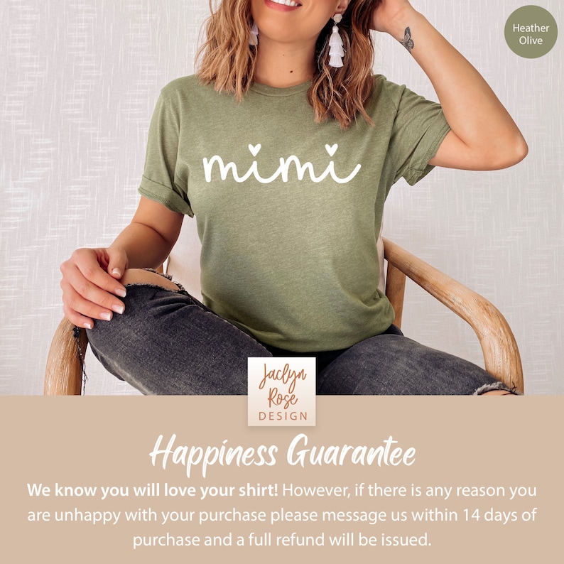 May include: A green t-shirt with the word "mimi" written in white with two small hearts on either side of the word. The t-shirt is being worn by a person sitting on a wooden chair. The text "Happiness Guarantee" is written in white on a brown background below the image. The text "We know you will love your shirt! However, if there is any reason you are unhappy with your purchase please message us within 14 days of purchase and a full refund will be issued." is written in black below the guarantee text.
