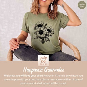 May include: Heather olive-colored t-shirt featuring a black and white sunflower bouquet design. The shirt includes the text "Jaclyn Rose Design" and "Happiness Guarantee". The shirt is made of a soft material.